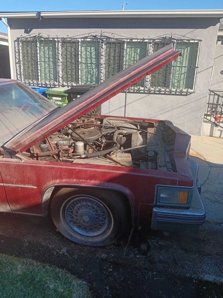 Close up of the engine bay and flat front tire of a maroon 1970s classic Cadillac project car parked in a Los Angeles driveway. Go Car Buyer pays cash for non-running vehicles.