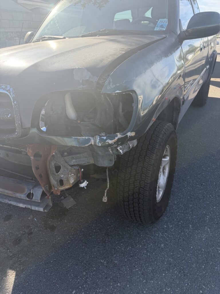A used dark green truck with heavy front-end damage purchased for cash by GoCarBuyer in San Bernardino, California