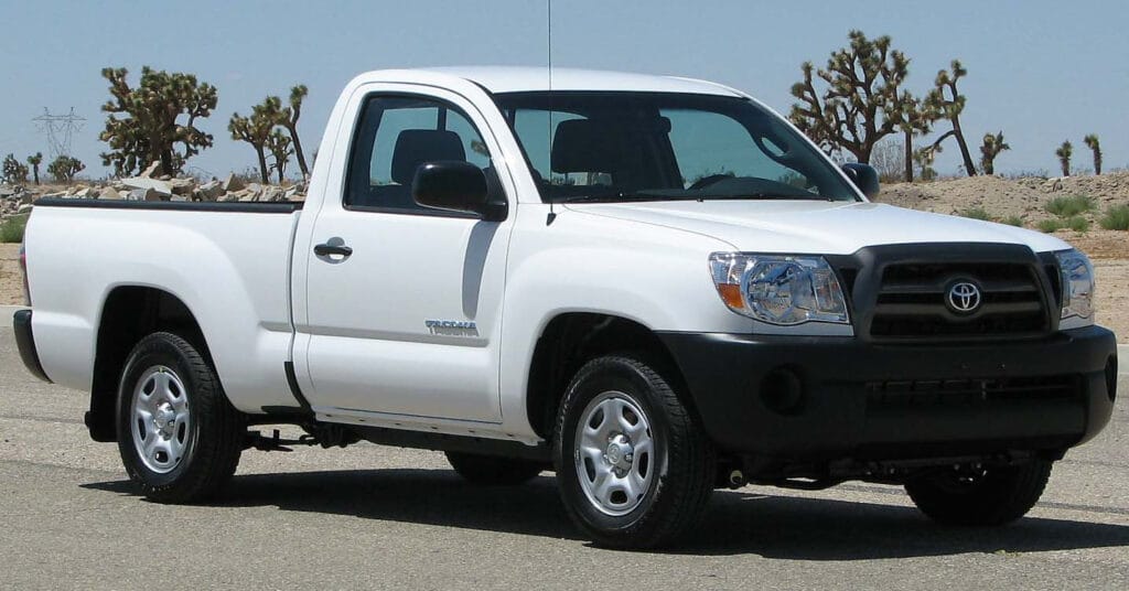 A clean 3/4 front view of a white base model 2nd generation Toyota Tacoma truck parked in a Southern California desert landscape. Go Car Buyer pays top cash for reliable Toyota trucks.