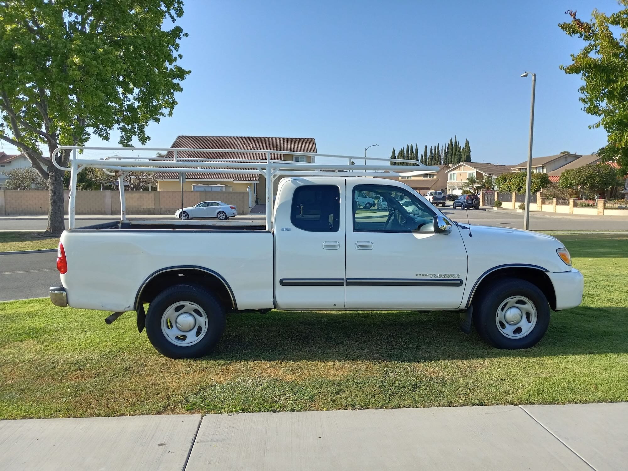 A clean white first-generation Toyota Tundra extended cab pickup truck featuring a professional white metal ladder rack. Go Car Buyer pays cash for modified and used work trucks.