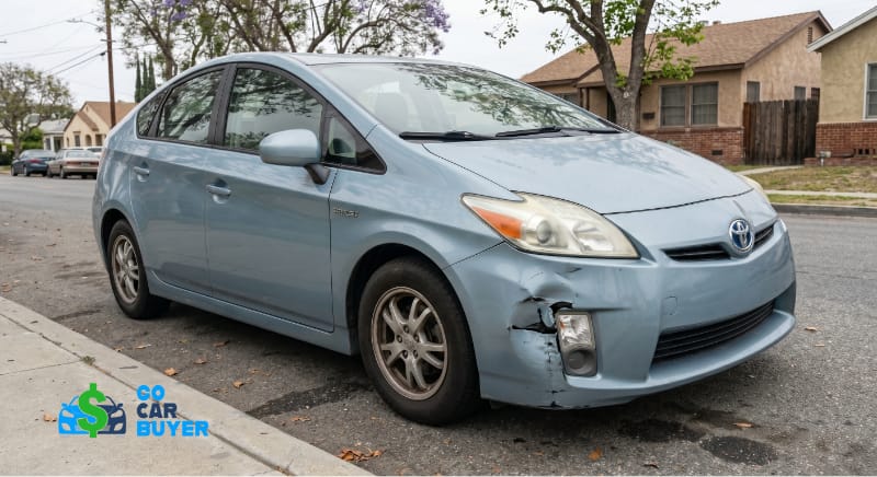 A light blue 3rd generation Toyota Prius with front bumper damage parked on a residential street in Anaheim. GoCarBuyer pays cash for damaged and high-mileage hybrids.