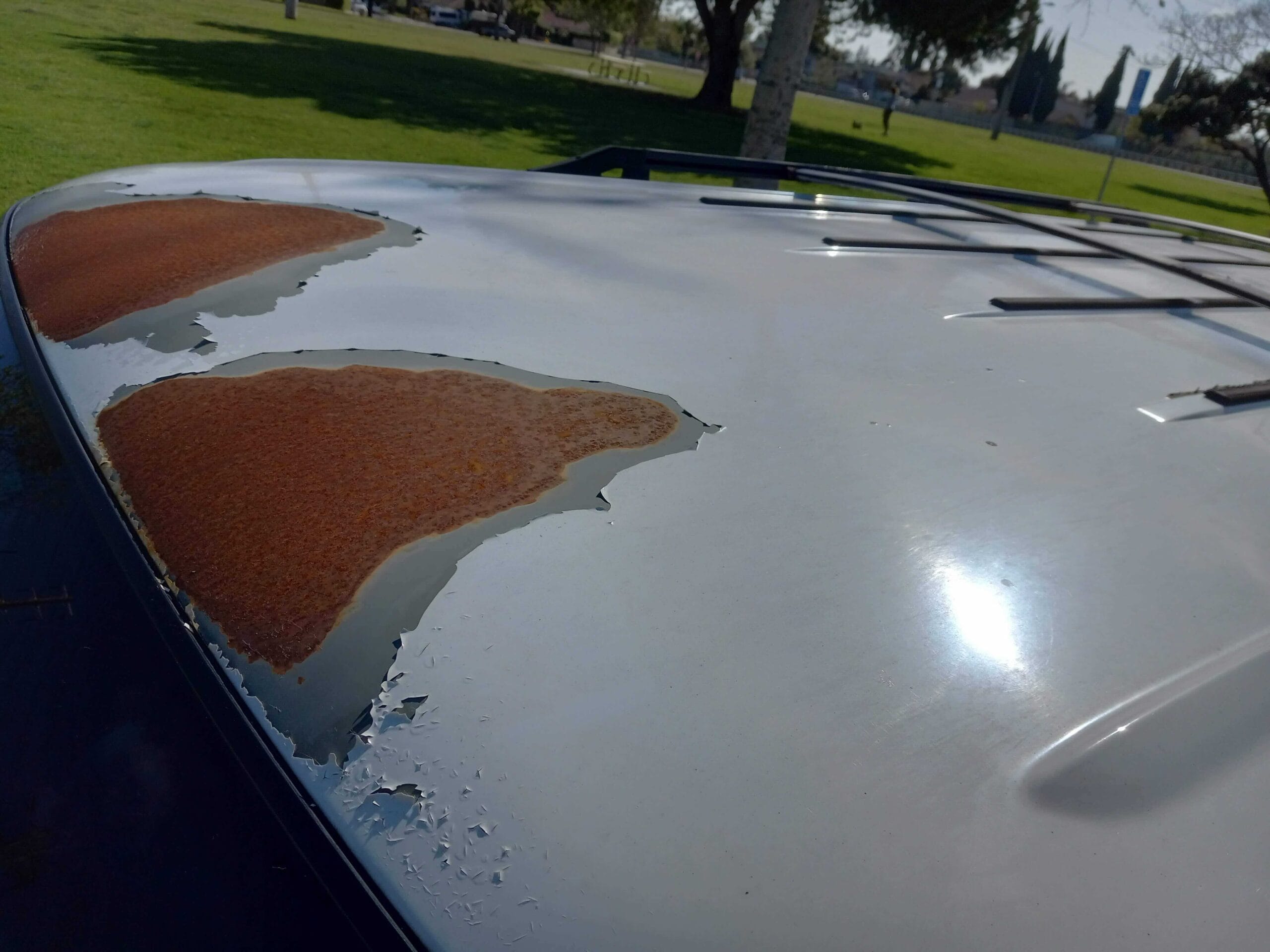 A close-up of a white vehicle roof showing severe peeling paint and large patches of orange surface rust. Go Car Buyer buys rusted cars for cash in Southern California.