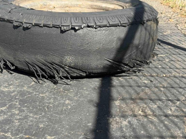 A severely shredded car tire with exposed steel belts and torn rubber. Go Car Buyer pays cash for undriveable vehicles.