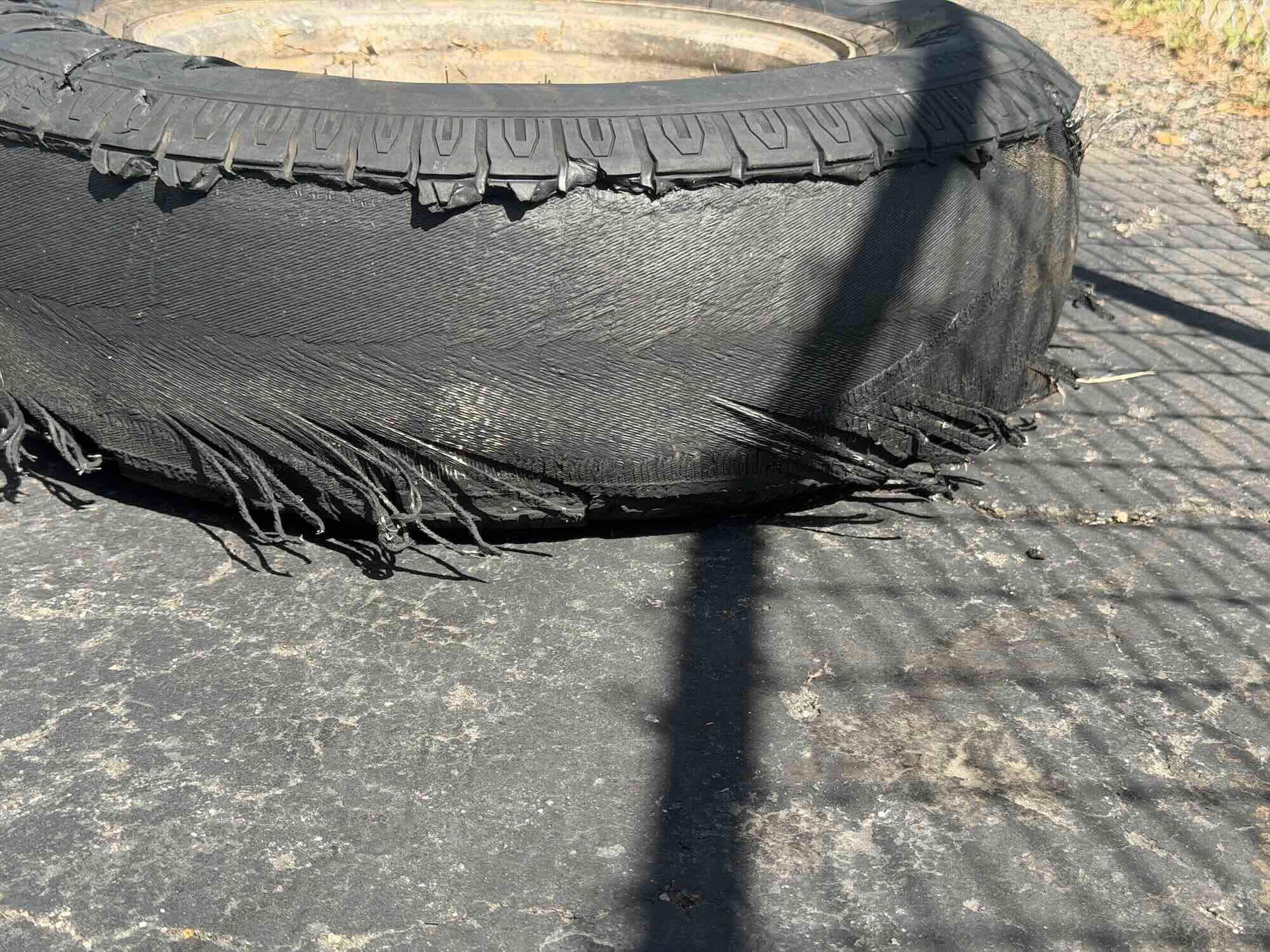 A severely shredded car tire with exposed steel belts and torn rubber. Go Car Buyer pays cash for undriveable vehicles.