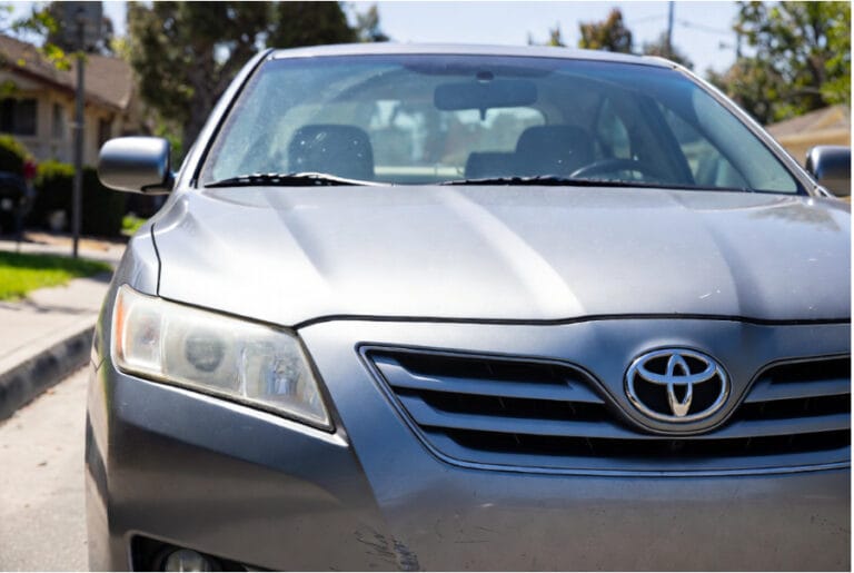 Close up of a silver 2007-2011 Toyota Camry with hazy headlights and bumper scratches parked on a residential street. GoCarBuyer pays cash for older and high-mileage Toyotas across Southern California.