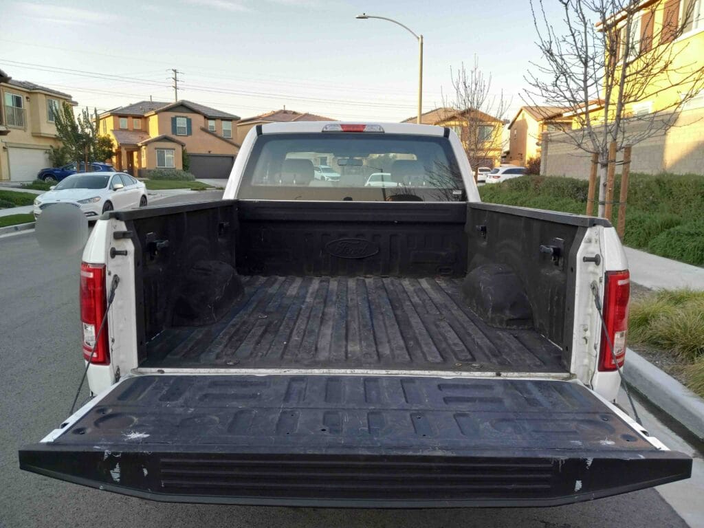 Clean, empty bedliner of a white Ford work truck with the tailgate down, ready to be sold.