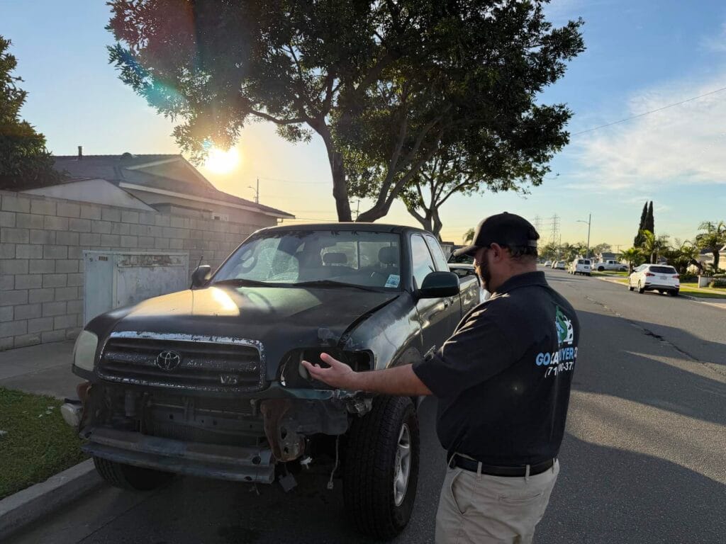 Accident damage on a dark green Toyota Tundra truck, which is missing its front bumper and headlight assembly. This is an example of a vehicle GoCarBuyer will buy for cash and rusted frame and missing bumper.